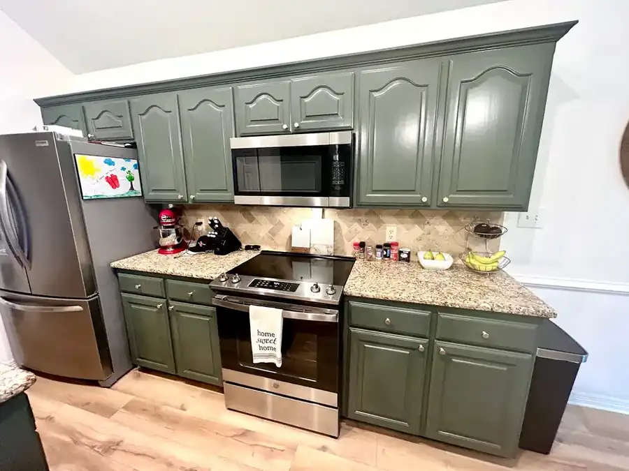 A finished kitchen: sage green painted cabinets, granite, stone backsplash and a light plank floor